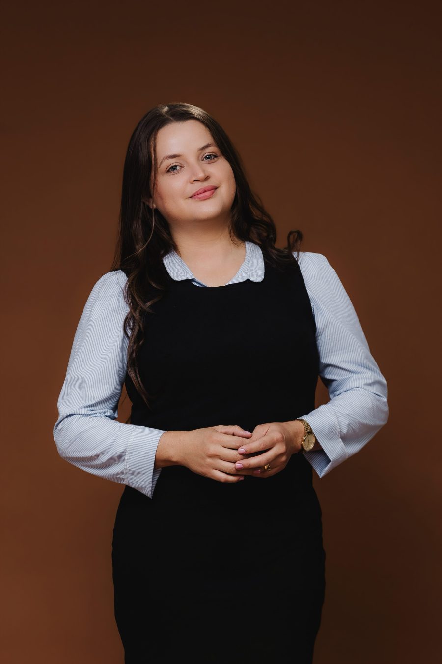 Claudiane Albarracin, psicóloga, em retrato profissional de pé, com as mãos entrelaçadas.